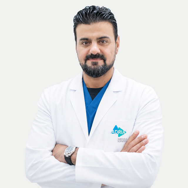 Medical doctor with arms crossed, wearing white coat and blue scrubs, logo on coat reads ADRIA Medical Centered photo.